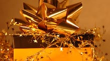 View of the top of a boxed gift with a gold bow, background, and garland with stars.