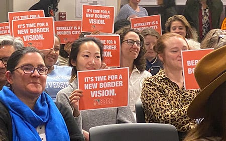 People holding up "It's Time for a New Border Vision" signs at the city council meeting