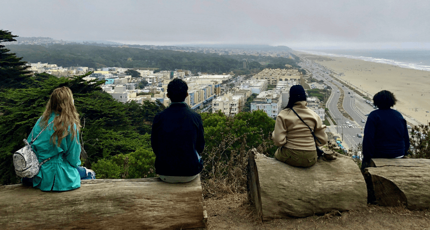students sitting on logs overlooking city and beach