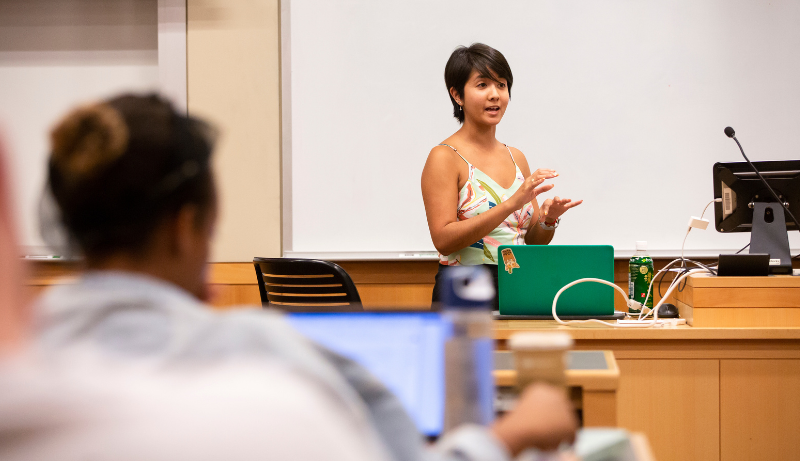 Stephanie Campos-Bui teaching seminar in front of green laptop, wearing white tank top