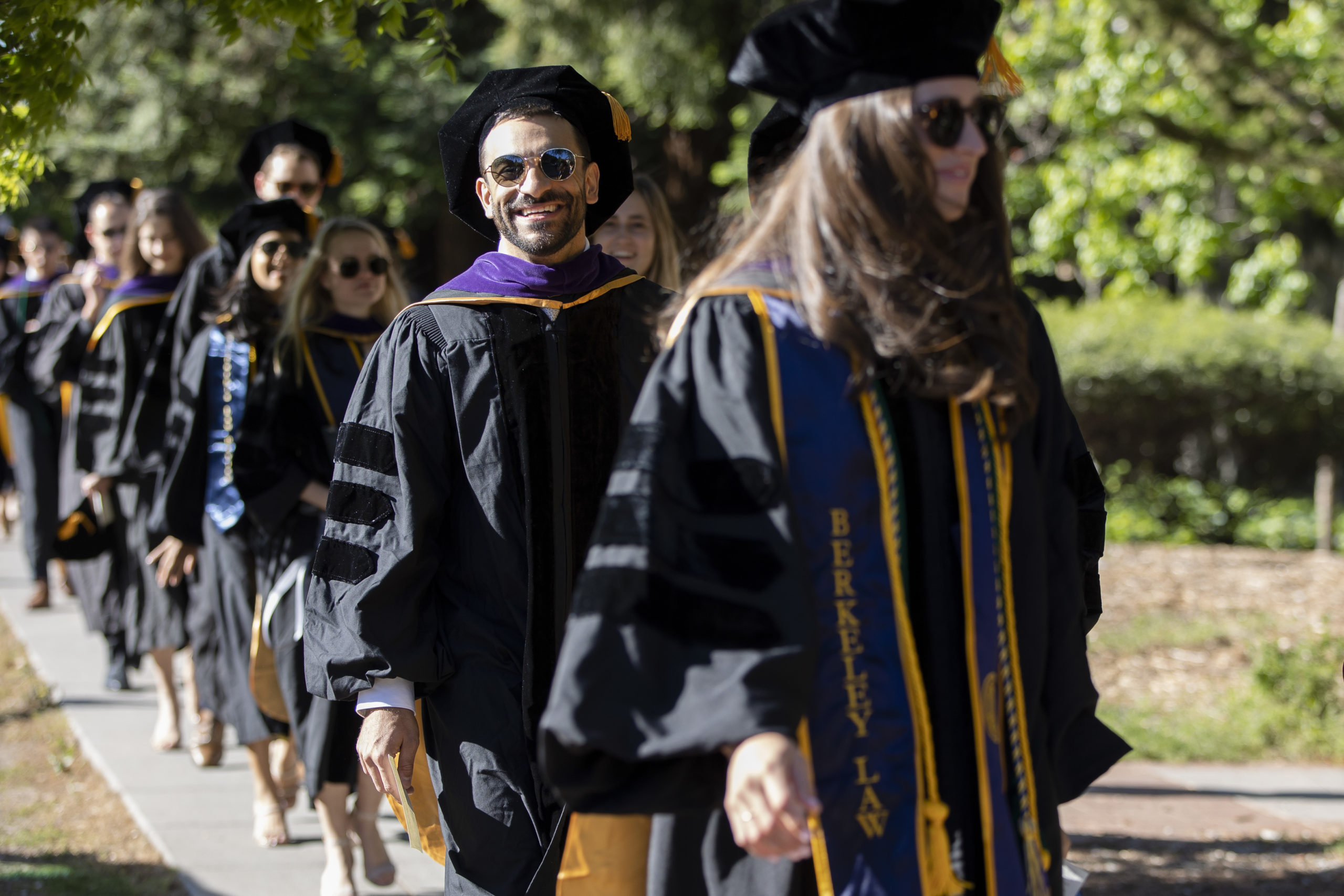 Students walking in a line wearing commencement regalia.