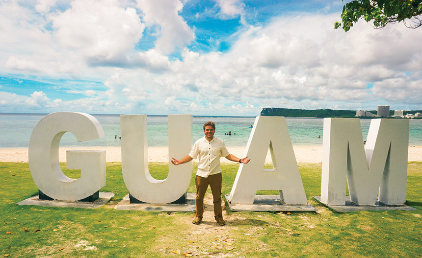 Felix in front of Guam sign at beach.