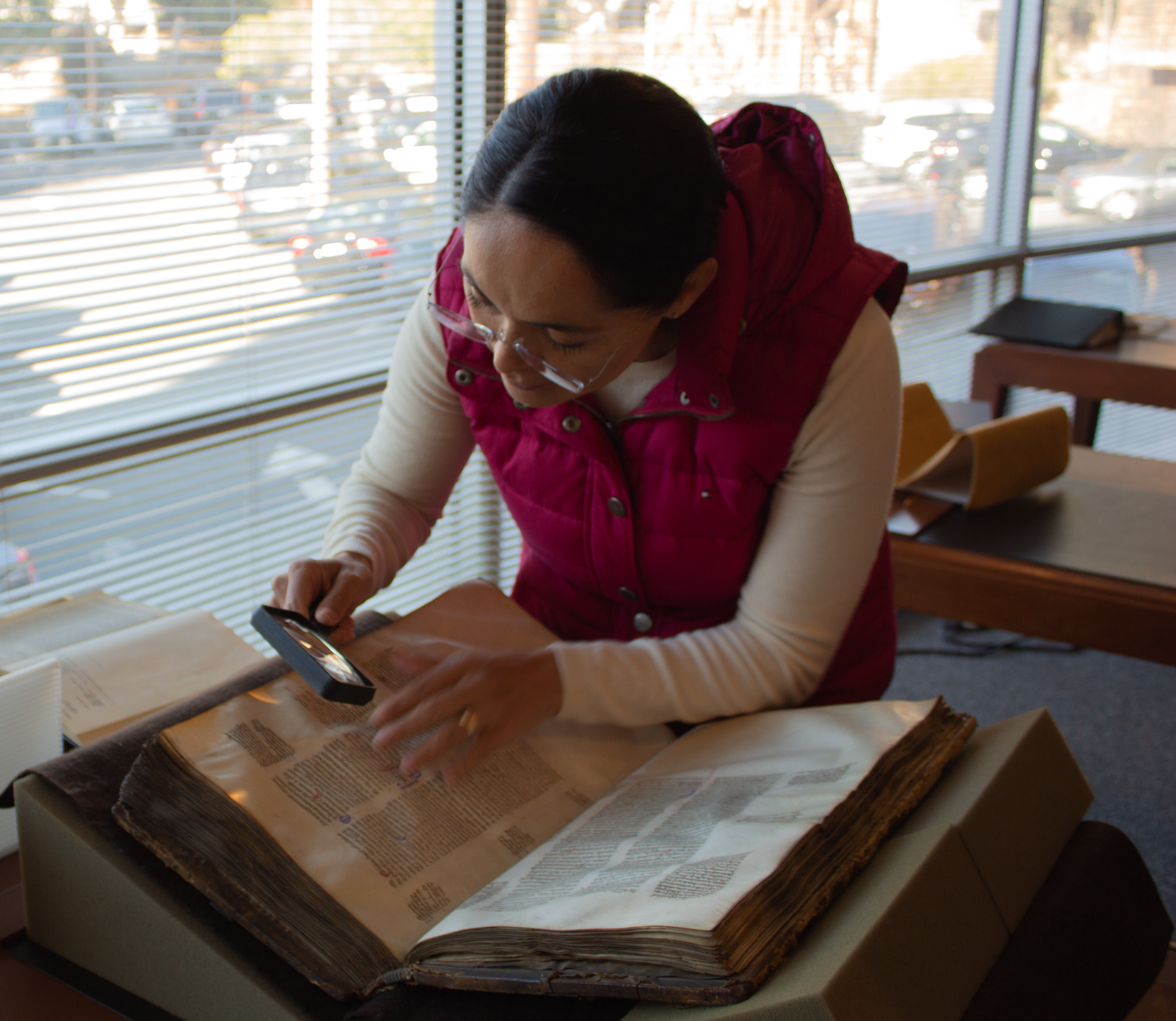 Photograph of Laura Velázquez Arroyo using a magnifying glass to look at a manuscript
