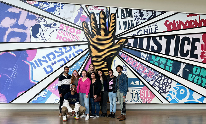 Students standing in front of mural with hand and messages of justice