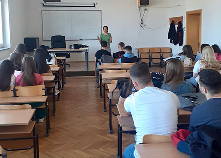 Tam in front of classroom with desks and students