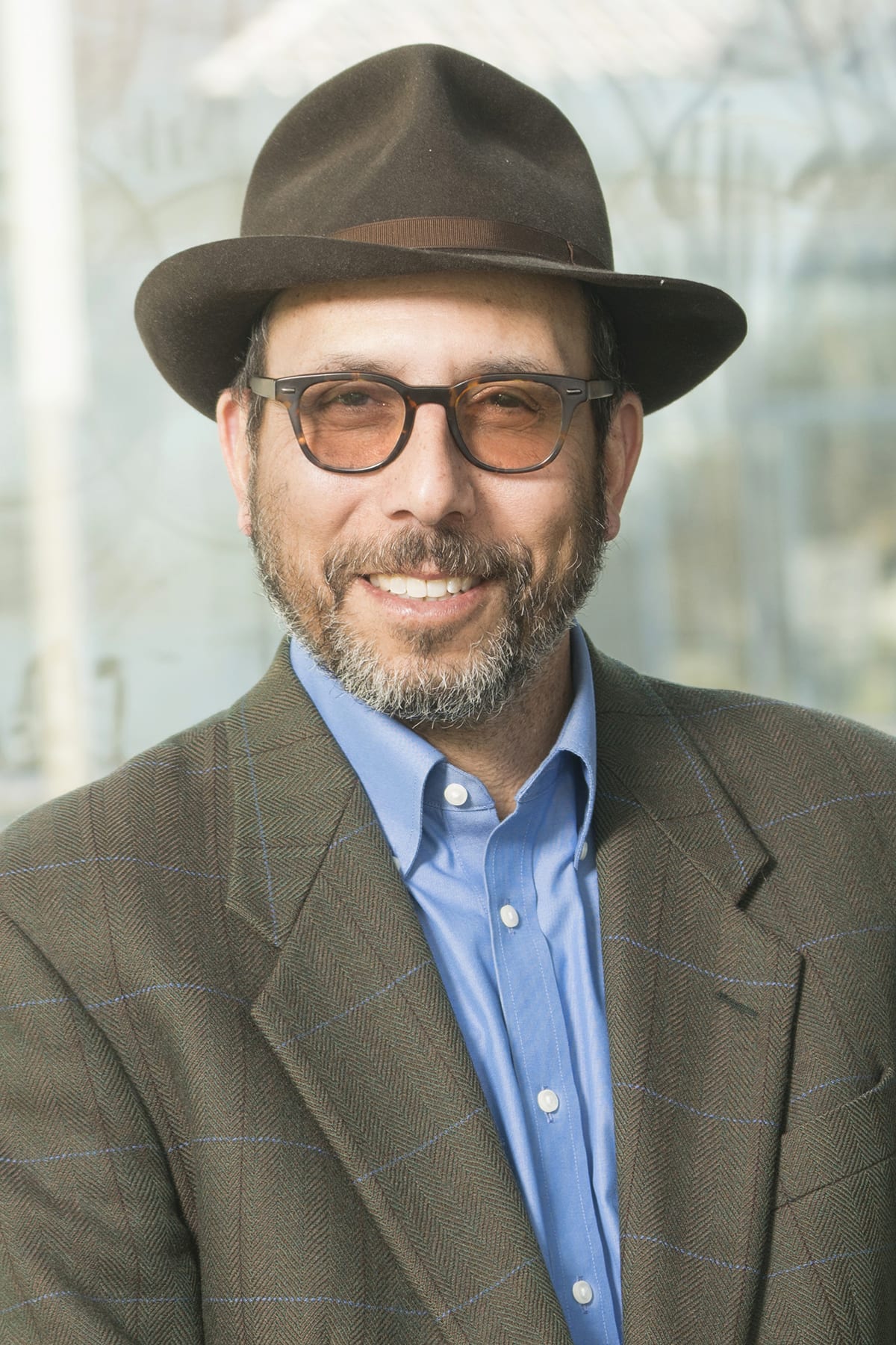  Jonathan Simon's headshot. Jonathan wears a tweed blazer, blue button up, brown hat, and glasses.