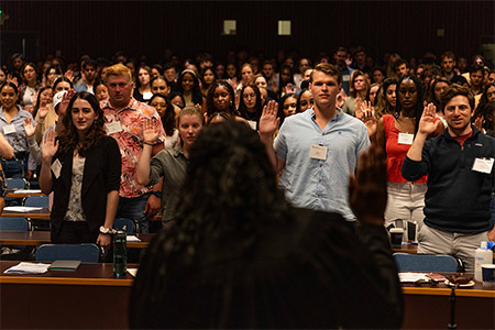 Students in auditorium raising right hand to take oath