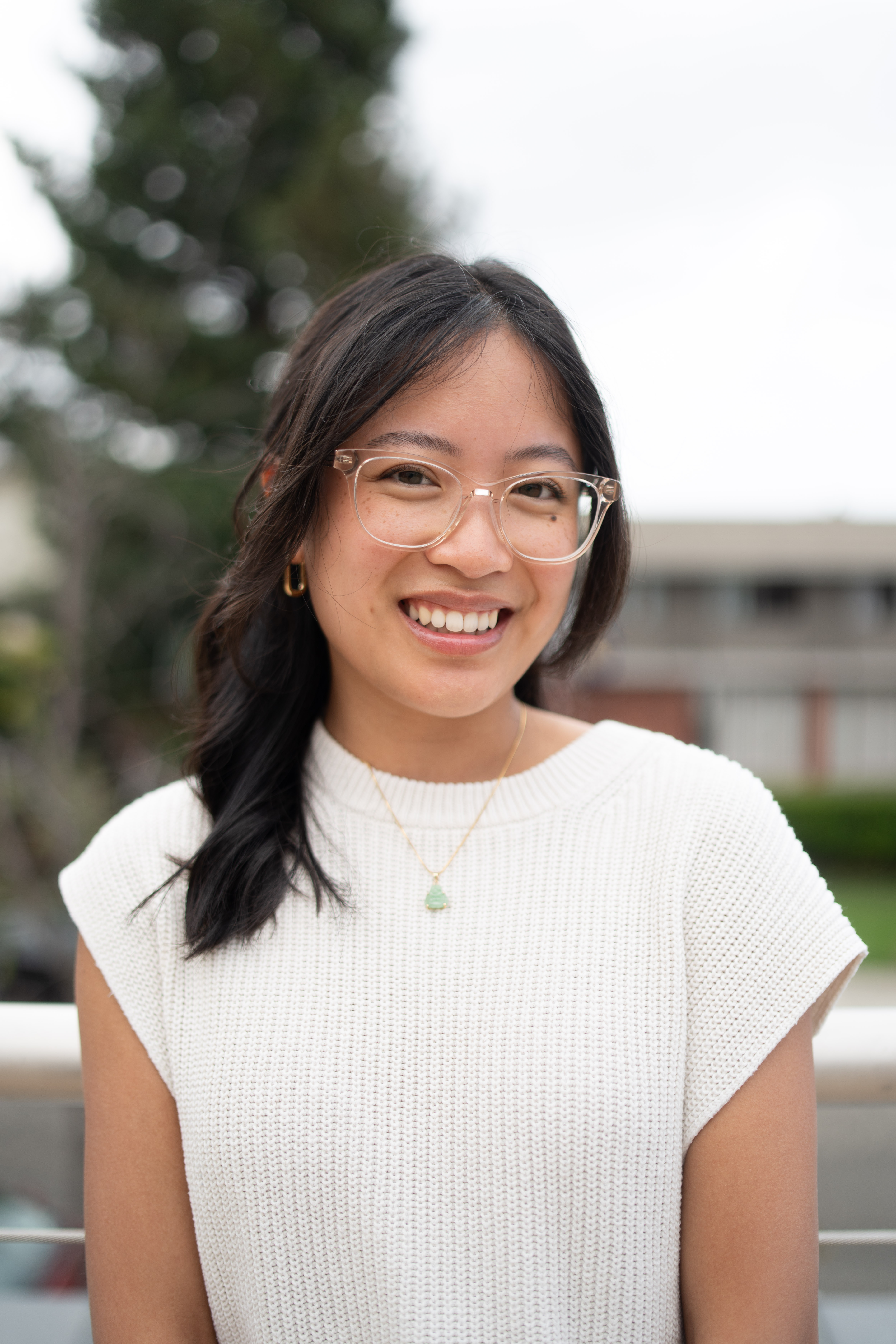 Cindy Nguyen's headshot. Cindy smiles a big smile in front of a tan wall. She is wearing a black sweater and has half-up, curly black hair.