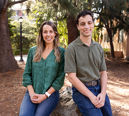 Two students outside leaning on a rock