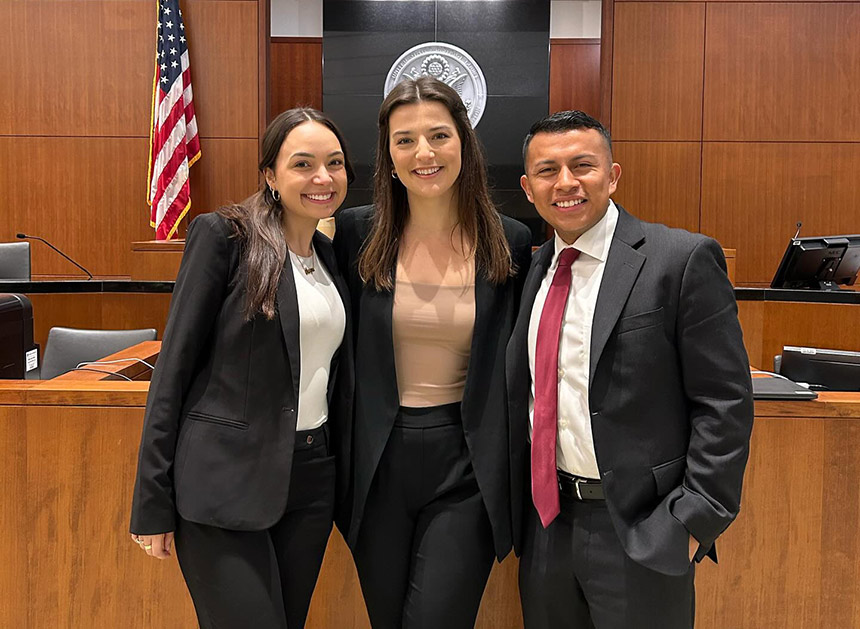 Three professionally dressed students posing in courtroom