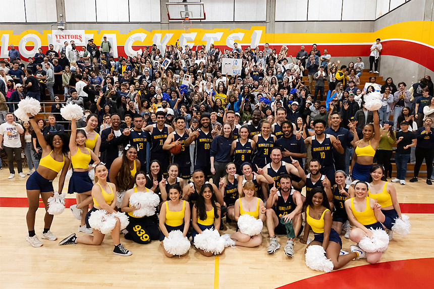 Large group of players and cheerleaders posing in blue and gold uniforms in a gymnasium