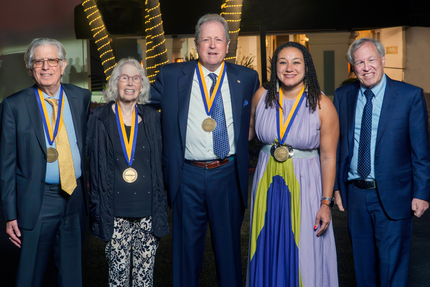 five people standing together and smiling, four with medals
